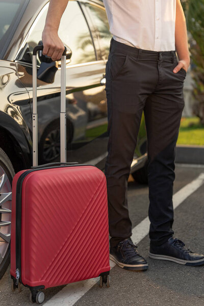 Man with a red luggage bag next to the black car. The concept of airport transfer or taxi