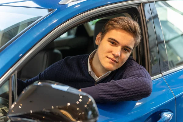 Retrato de un joven cliente sentado en un coche nuevo. Comprar un vehículo en un concesionario — Foto de Stock