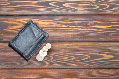 Koyu renk ahşap arka planda birkaç Euro madeni parası olan siyah cüzdan.