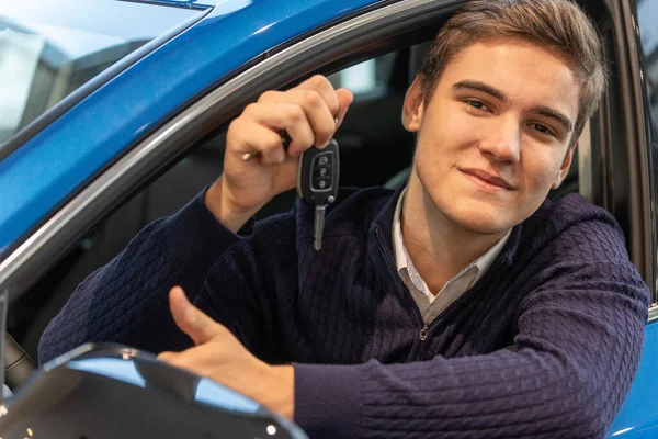 Retrato de un hombre feliz que compró un coche nuevo. Un joven mostrando llaves mientras está sentado en un vehículo — Foto de Stock