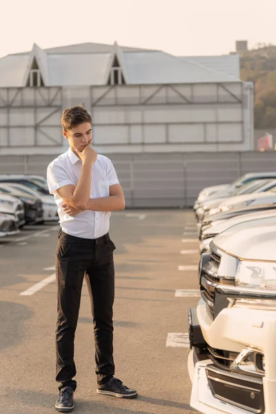 Adolescentul stă și se gândește să aleagă o mașină nouă la dealer. Cumpărarea unui vehicul într-un spectacol auto — Fotografie, imagine de stoc
