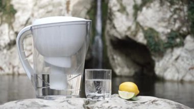 Bir dağ şelalesinin arka planında kireç ve bir bardak saf suyu filtrele
