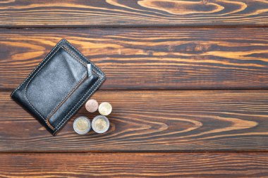 Koyu renk ahşap arka planda birkaç Euro madeni parası olan koyu deri bir cüzdan. Yukarıdan manzara. Düz yatıyordu