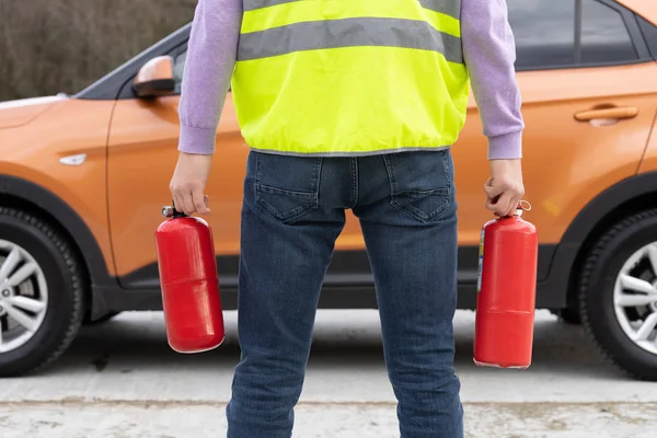 En man med två brandsläckare i handen nära bilen. Fokus på brandsläckare. — Stockfoto