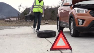 Yansıtıcı yelek giyen bir tamirci yolda tekerleği değiştirir.