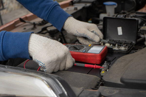 Механик с помощью вольтметра проверки напряжения аккумулятора в автомобильном сервисном центре
