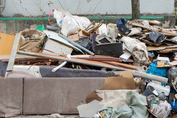 Konut binasının avlusunda farklı türde çöp yığını, plastik torbalar ve çöp bidonları var. Çevre kirliliği ve kamusal alan