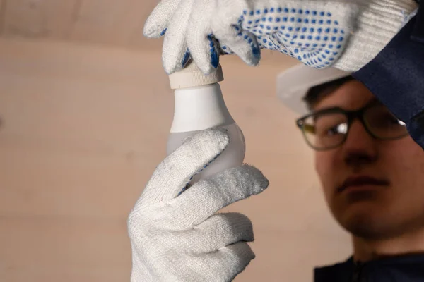 Profesyonel bir elektrikçi ampulü değiştiriyor. Adam yeni bir ampulü tavan lambasına sokuyor. Yakın plan.