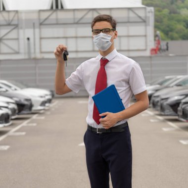 Yüzünde tek kullanımlık koruyucu maske olan bir araba galerisinin satış müdürü.