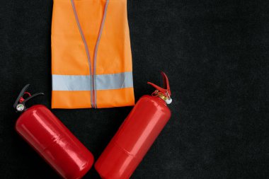 İki kırmızı yangın söndürücü ve koyu arkaplanda turuncu yansıtıcı bir yol yeleği. Boşluğu kopyala