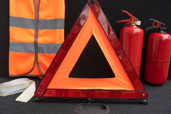 Elements of the essentials for a passenger car: manual fire extinguisher, folding emergency automobile traffic warning stop sign, high-visibility vest, tow rope