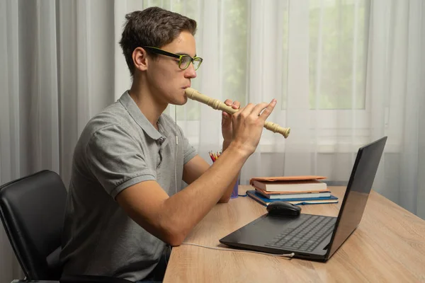 Kulaklıklı genç adam internette flüt çalma eğitimi alıyor. Uzaktan eğitim. Uzaktan müzik aletleri çalmayı öğrenme