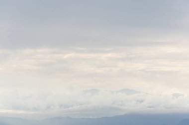 Bulutlu gökyüzü ve bulutların arasından bakan dağlar.