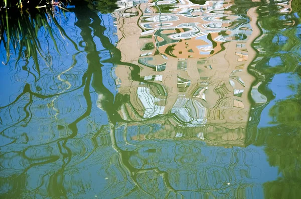 Reflexão de uma árvore e de um edifício distorcido pelo movimento da água — Fotografia de Stock