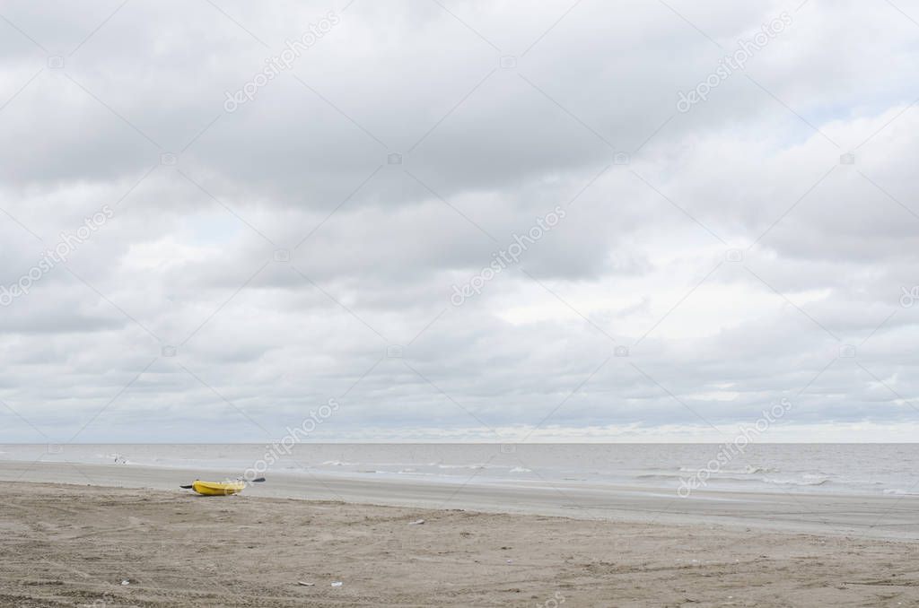 Beach landscape without people, a kayak in the sand, a calm sea and a cloudy sky