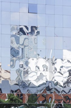 Çevresindeki yapıların yansıtıldığı, deforme olduğu yansıtıcı duvar.