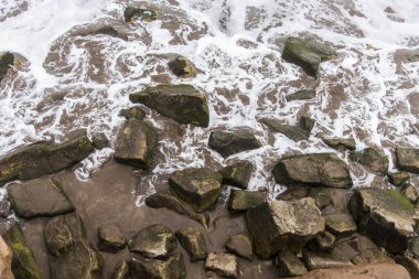 Sahildeki kayaların arasında çırpılmış, beyaz köpüklü deniz suyu. Üst görünüm.