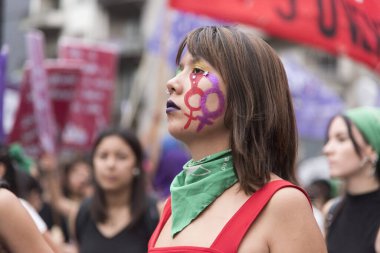 CABA, Buenos Aires / Argentina; March 9, 2020: international women's day. Serious expression young woman, wearing makeup and a green handkerchief, on the march, national women's strike