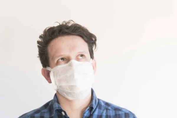 Frontal portrait of a young man looking up, wearing a disposable face mask, to prevent the spread of coronavirus disease, Covid-19