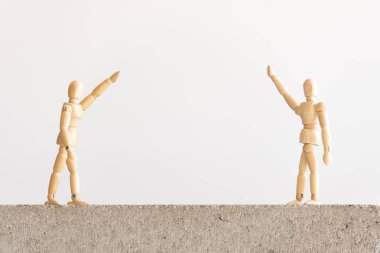 Sosyal uzaklık sembolü: iki ahşap insan figürü beton bir blokta duruyorlar ve aralarında iyi bir ayrılık var, el sallıyorlar