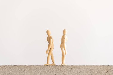 Sırtları birbirine dönük beton bir blokta duran iki tahta insan figürü.