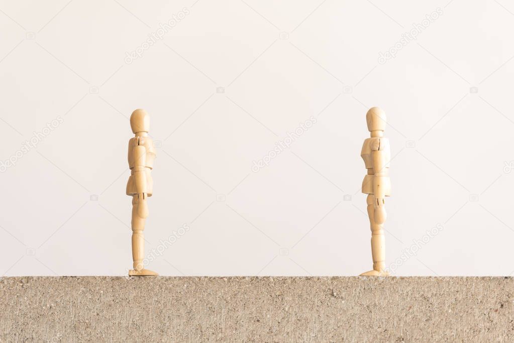 Social distancing symbol: two wooden human figures standing on a concrete block looking at each other with a good separation between them.