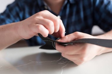 Eller sentetik deri parçaları dikiyor, Coronavirus salgını bağlamında covid-19 'un yayılmasını önlemek için ev yapımı koruyucu yüz maskesi yapıyor..