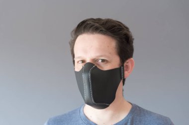 Coronavirus hastalığının yayılmasını önlemek için ev yapımı sentetik deri koruyucu yüz maskesi takan genç bir adamın portresi..