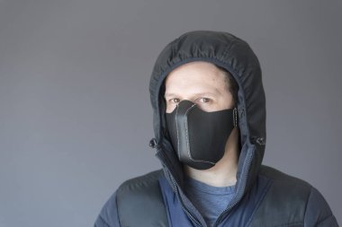 Coronavirus 'un salgını bağlamında yayılmasını önlemek için ev yapımı sentetik deri maske takan genç bir adamın portresi. Ceket giyiyor, kışlık giysiler.