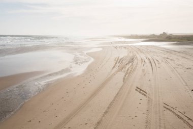 Gün batımında Cabo Polonio, Rocha, Uruguay 'da ayak izleri ve kamyon izleri olan plaj.