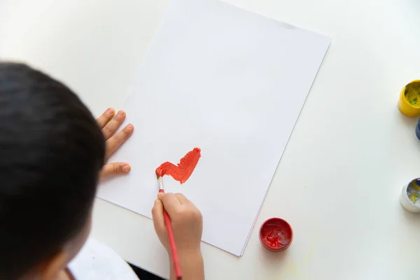 Little boy hand draws on paper. Cute Child boy is sitting and painting. Stay home.