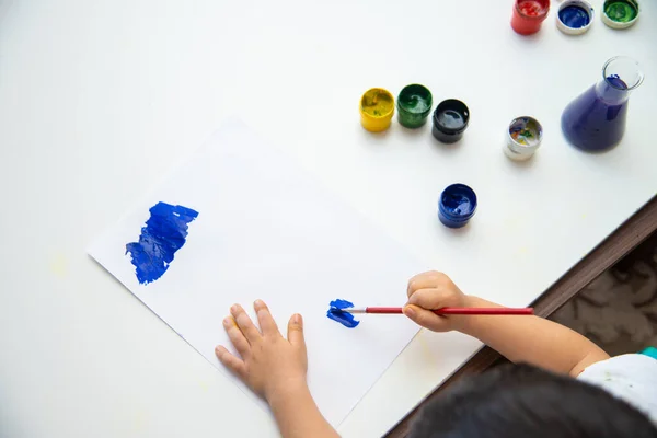 Little boy hand draws on paper. Cute Child boy is sitting and painting. Stay home.