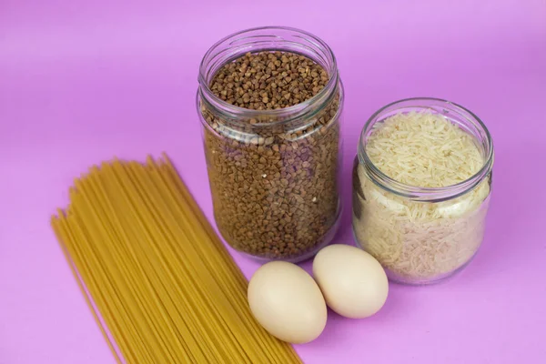 Food stock for quarantine isolation period on purple background. Rice, egg, buckwheat, spaghetti. Food delivery, Donation. Copyspace