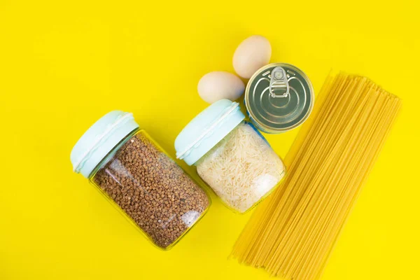 Food stock for quarantine isolation period on yellow background. Rice, egg, canned food, buckwheat, spaghetti. Food delivery, Donation. Copyspace