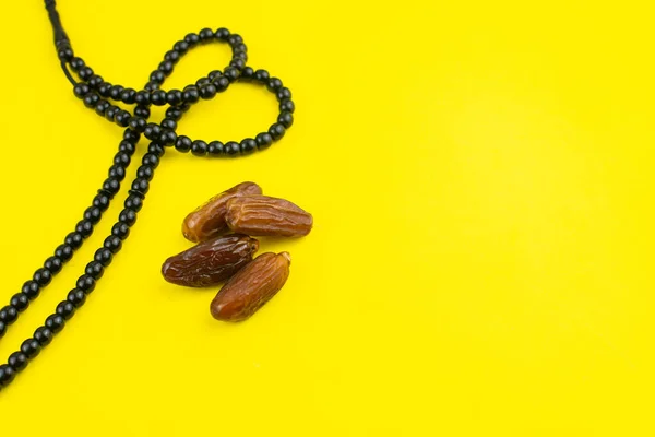 Ramadan Kareem Festival. Close up of dried dates fruit in bowl with rosary on yellow background. Copy space.