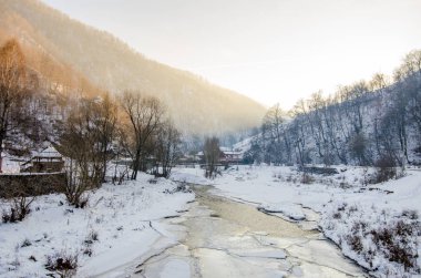 Soğuk bir kış gününde Transilvanya kırsalındaki kırsal bir köyden akan donmuş bir dere.