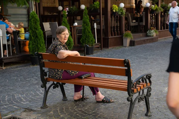 Chernivtsi, Ucraina, 25.08.2019: Vecchia seduta su una panchina vicino a caffè di strada nel centro della città — Foto Stock