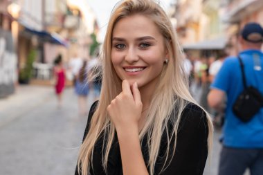 Chernivtsi, Ukrayna, 25.08.2019: Blacak elbiseli mutlu sarışın kız eski kentin yayaların arasında duruyor ve elini başının yanında tutuyor