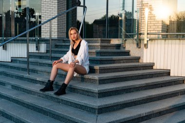 Açık havada, beyaz gömlekli, siyah çizmeli güzel sarışın bir kızın portresi.