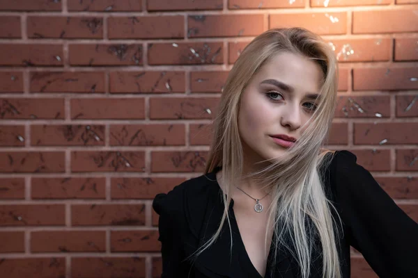 Gros plan portrait d'une belle fille blonde aux cheveux lâches, lèvres rouges et yeux bleus regardant la caméra, mur de briques rouges sur le fond — Photo