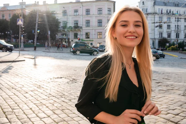 Chernivtsi, Ukraine, 25.08.2019 : Joyeux jeune femme blonde en robe noire souriante et marchant dans les rues de la vieille ville — Photo