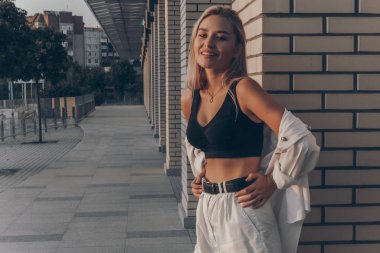 Beyaz şort ve gömlek giymiş, belinde açık sarı saçları olan çekici, şık bir genç kadın.