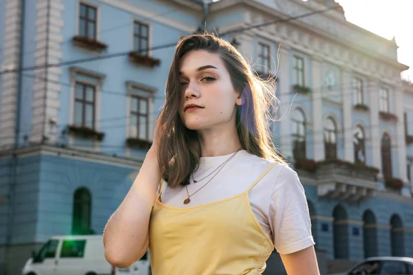 Ελκυστική νεαρή καστανή κοπέλα με φυσικό μακιγιάζ ντυμένη με κίτρινο t-shirt αγγίζοντας τα μαλλιά της με το χέρι της και κοιτάζοντας την κάμερα — Φωτογραφία Αρχείου