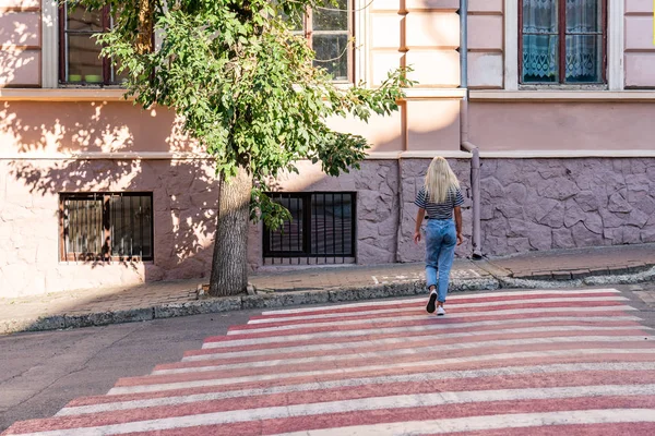 Estate ritratto soleggiato della giovane attraente viaggiatrice bionda in t-shirt grigia e jeans blu sulla passerella rossa tra il centro storico della città — Foto Stock