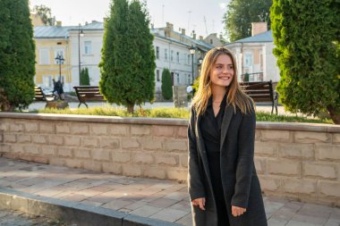 Siyah pelerinli mutlu gülen kız gezgin eski şehir meydanının arasında duruyor.