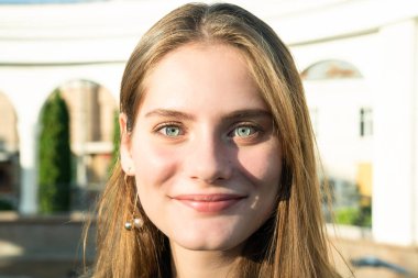 Mavi gözlü, doğal makyajlı ve yüzünde güneş ışınları olan mutlu esmer kızın yakın portresi.