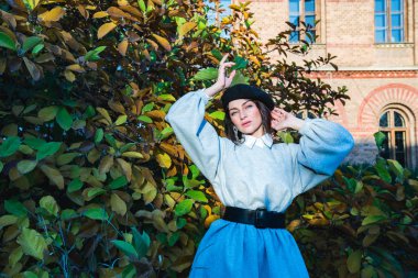 Siyah bereli ve gri elbiseli güzel gizemli kız sonbahar çalılarının yanında duruyor.