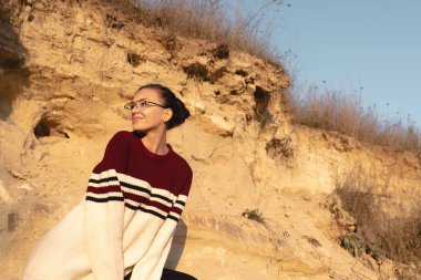 Kırmızılı esmer kızın sonbahar güneşli portresi ve kumların arasında güneş gözlüğü.