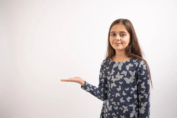 Cintura até retrato da jovem morena atraente em vestido azul que fica com a palma aberta levantada, segura o seu produto e olhando para a câmera, isolado sobre fundo branco — Fotografia de Stock