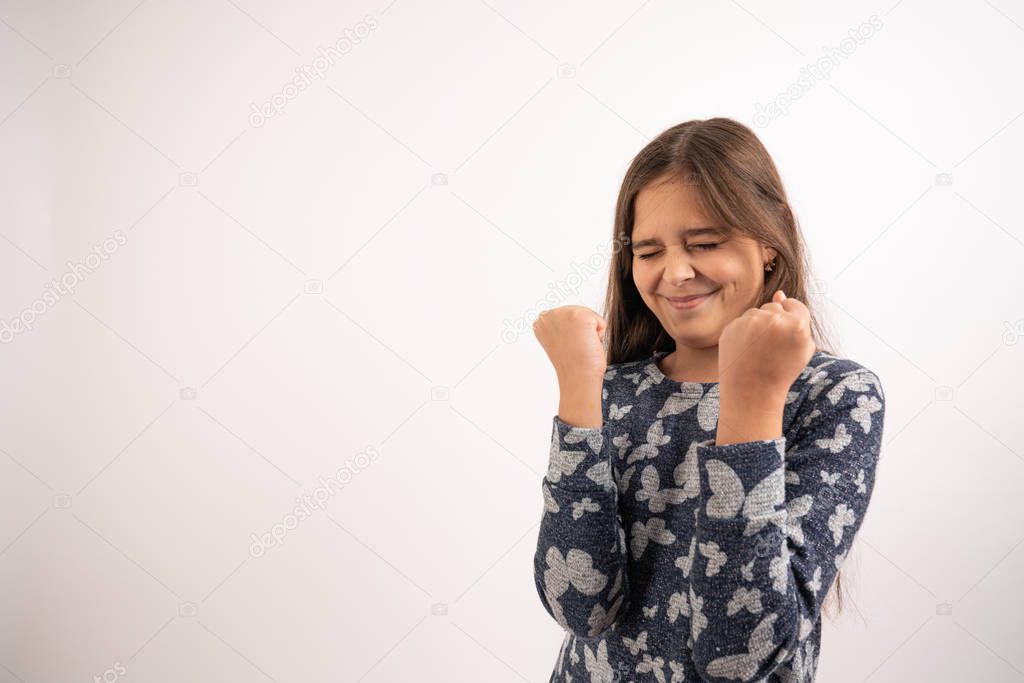 Waist up portrait of the beautiful brunette girl with loose hair dressed in blue shirt stands with clenched fists, emotions of success and trial